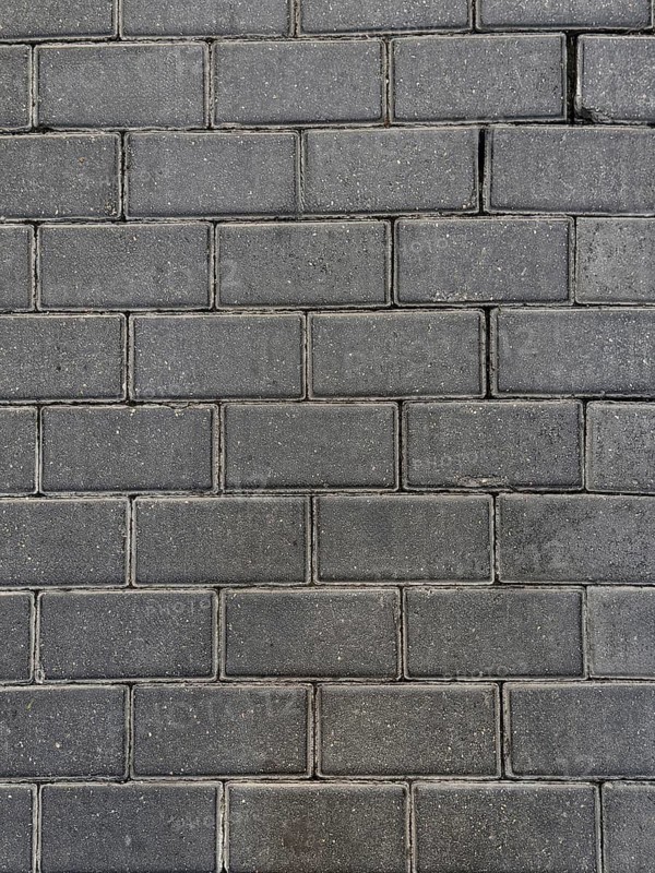A close-up view of a dark stone brick wall, showcasing its rough texture and the pattern formed by rectangular bricks. Ideal for backgrounds in architecture and construction themes