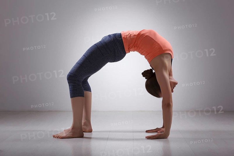 Beautiful sporty fit yogini woman practices yoga asana chakrasana (or urdva dhanurasana), wheel pose (or upward facing bow) pose in studio
