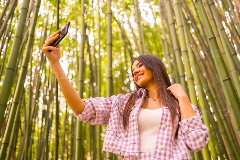 Young caucasian girl with a pink skirt in a bamboo forest. Enjoying summer holidays in a tropical climate, a girl lifestyle doing a selfie in the forest