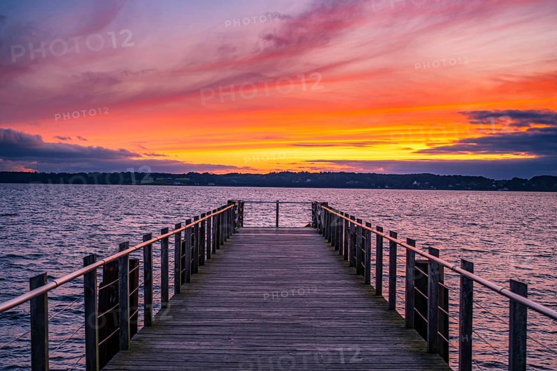 Wooden jetty juts into the sea during a spectacular sunset with intense colours in the sky, Glücksburg, Germany