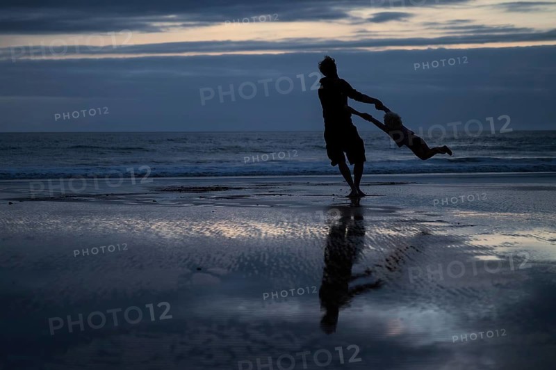 Silhouette of a man and a child playing on the beach after dark, Morocco
