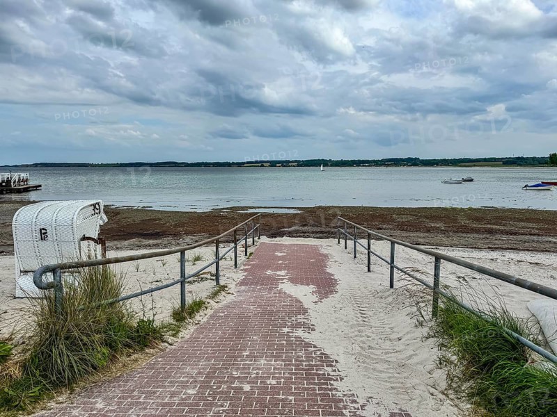 A paved access leads over sand to the Baltic Sea under a cloudy sky, Hohwacht, Schleswig-Holstein, Germany