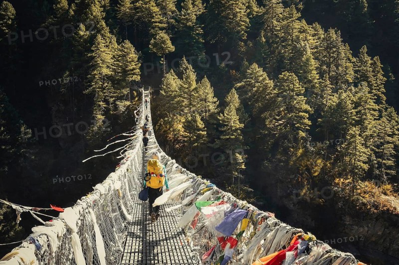 Caucasian woman trekking on famous bridge In Nepal outdoors surrounded by autumn nature. Chilly morning and travel outdoors in fall