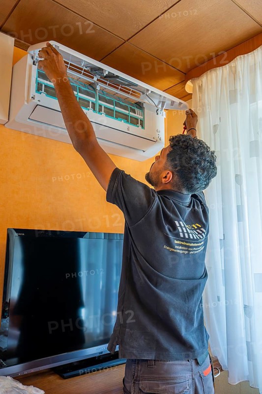 A man installs an air conditioner in the living room next to a television, air conditioning and refrigeration technology, private house, Wurmberg, Germany