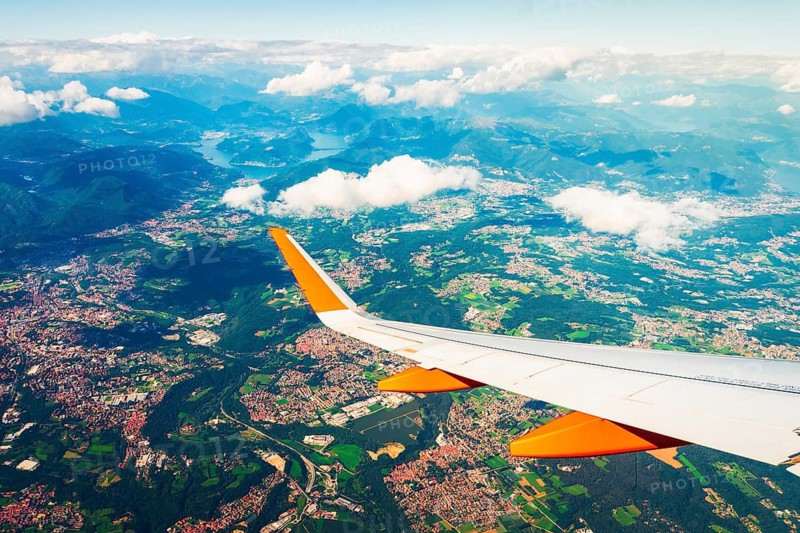 Aerial commercial aircraft passenger window seat point of view on take off. Airplane wing above towns farmland and mountains seen through aircraft window during flight travel transportation tourism