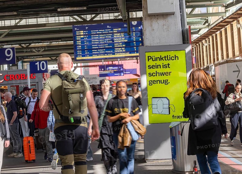 Being on time is hard enough. Advertising for the Fränk mobile app in Stuttgart Central Station. People on the platform. Stuttgart, Baden-Württemberg, Germany