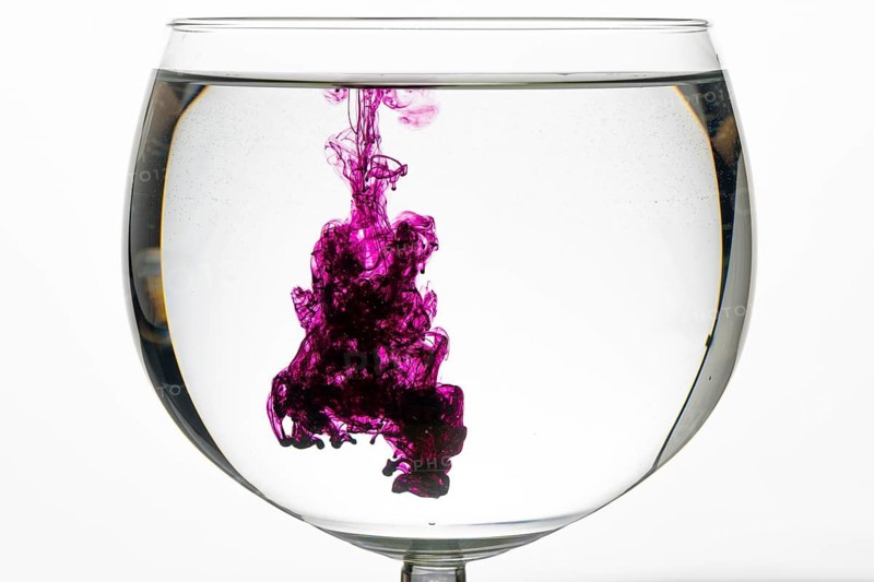 Violet ink mixes artistically in the clear water of a glass
