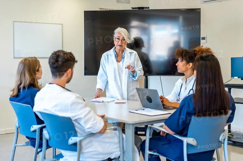 Experienced doctor explaining a new treatment to her colleagues during a medical training, using a laptop and a monitor