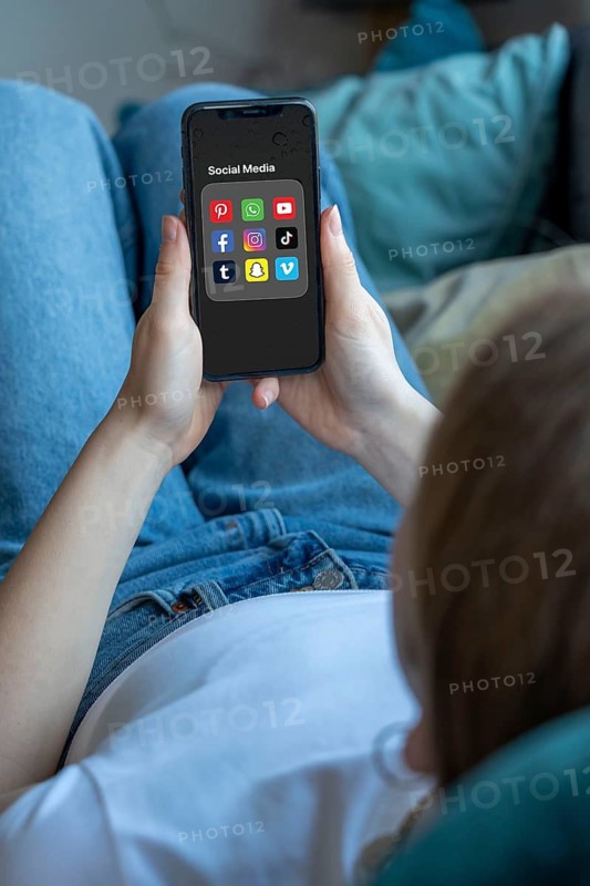 Symbolic image of social media use by young people, children, young woman, girl, 14 years old, folder with various social media platforms on the mobile phone