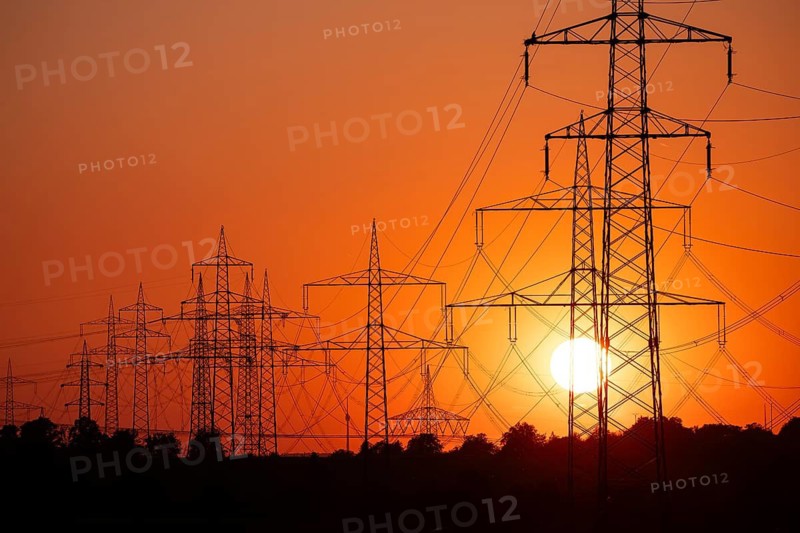 Silhouette of several high-voltage power lines and electricity pylons against a glowing orange and red sunset sky in Germany