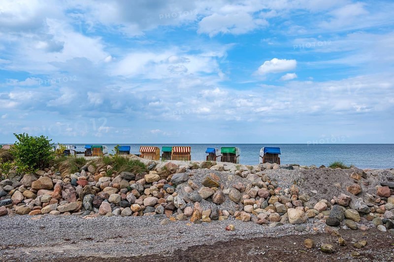 Beach chairs stand along a rocky coast under a partly cloudy sky, Hohwacht, Schleswig-Holstein, Germany