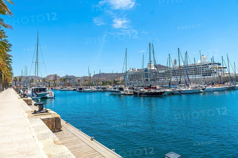 Cartagena port in murcia, spain, featuring numerous sailboats and a large cruise ship docked in the marina under a bright summer sky, offering a view of the city's coastal landscape
