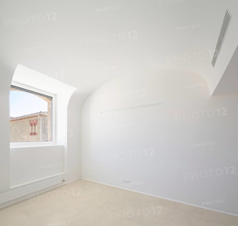 A spacious empty room of hospital with clean white walls, a large window providing natural light, and an arched ceiling. The minimalistic design exudes simplicity and modern elegance