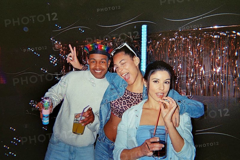 Diverse young adult friends confidently posing and enjoying a retro themed party with drinks, bubbles, and festive decorations, celebrating friendship and good times