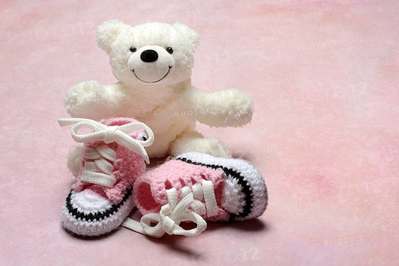 Pink baby shoes with teddy bear, pink background