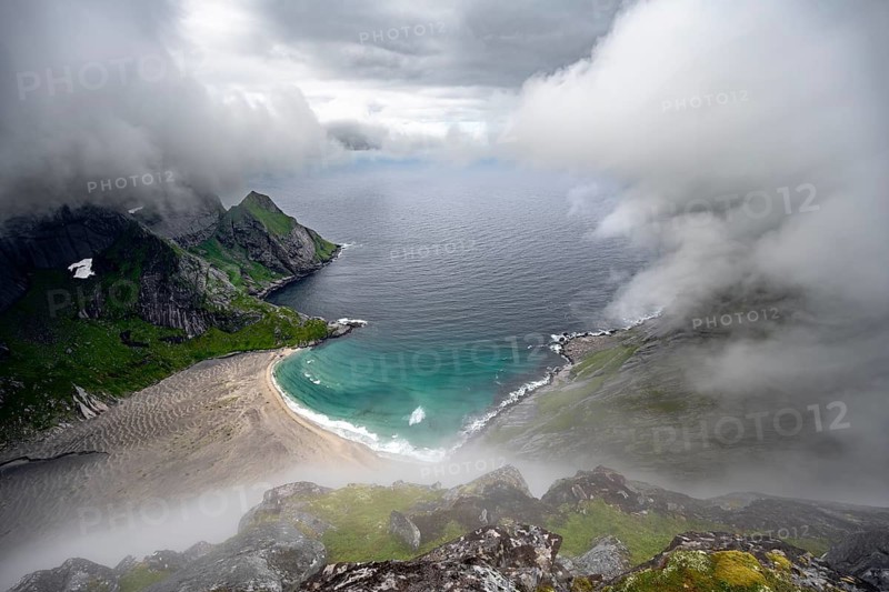 View from Helvetestinden summit, Bunesstranden sandy beach and blue sea, dramatic cloudy sky, Lofoten, Norway