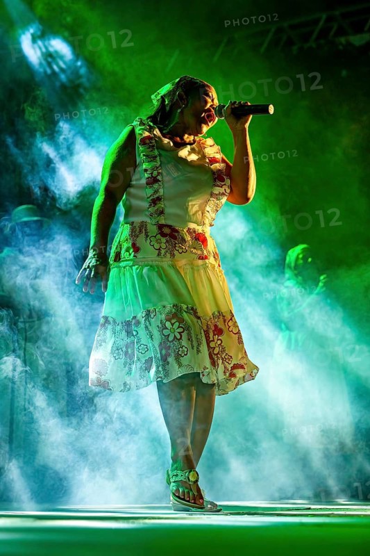 Woman dressed in floral patterns sings on stage in fog surrounded by expression and lights, a band plays and dances at a festival in Petrolina in Brazil