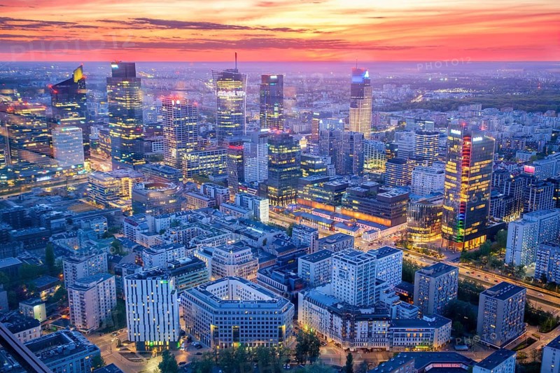Broad view across the Warsaw skyline in Poland with skyscrapers, city lights, glass high-rises, blue hour twilight and evening glow