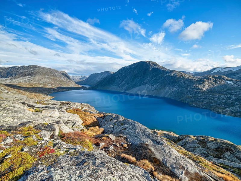 A calm lake surrounded by rocky mountains under a clear blue sky with clouds, view of Lake Djupvatnet, Dalsnibba pass road, mountain, autumn, Geiranger, Møre og Romsdal, Vestland, Norway