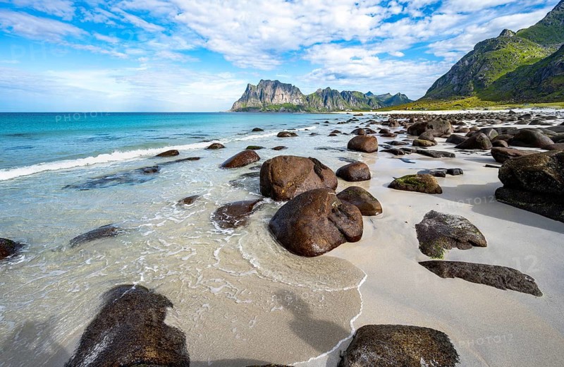 Rocks on the sandy beach of Uttakleiv, coast and blue sea, rocky mountain peaks, Vestvågøya, Lofoten, Nordland, Norway