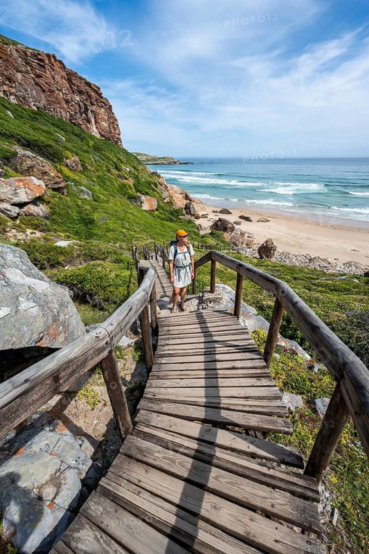 Young pretty woman wearing dress off coast and sea at Robberg Nature Reserve, Plettenberg Bay, South Africa