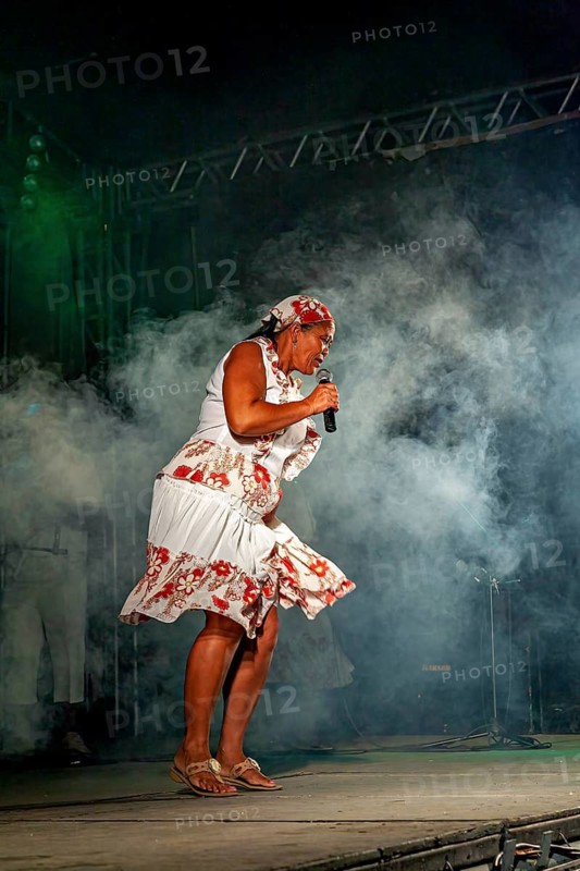 Woman singing on stage in a flowery dress surrounded by smoke, a band plays and dances at a festival in Petrolina in Brazil