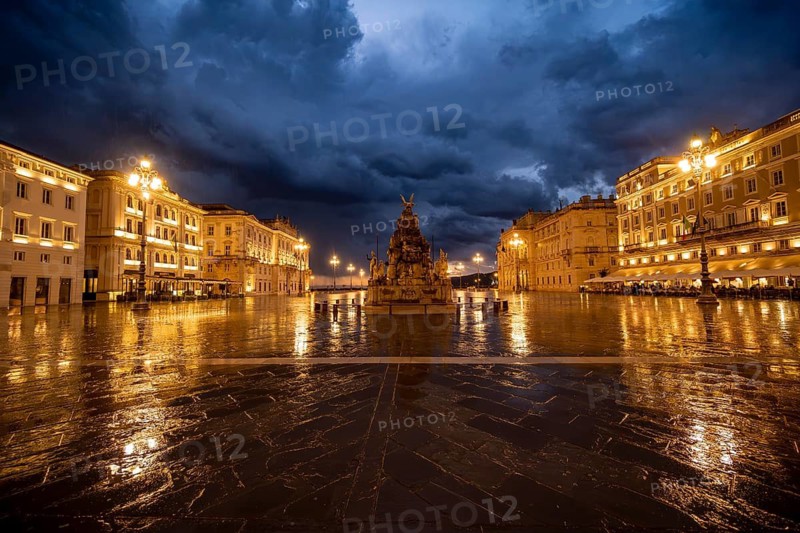 Illuminated square Piazza Unità d'Italia with Fontana dei Quattro Continenti fountain, Palazzo del Lloyd Triestino and Palazzo della Luogotenenza Austriaca or Palazzo Governo, with reflection, dramatic clouds, blue hour, old town, Trieste, Friuli-Venezia Giulia region, Italy