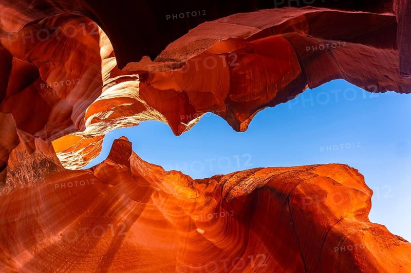 Swirling sandstone formations inside a famous slot canyon creating a natural frame for the bright clear blue sky, illustrating the impact of water and wind erosion on the earth over time