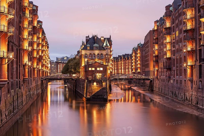 11.6.2018: Twilight view of the Wasserschloss (Water Castle) in the historic Speicherstadt district. The illuminated red brick warehouse complex and the canal are reflected in the water during the blue hour. UNESCO World Heritage site, Hamburg, Germany