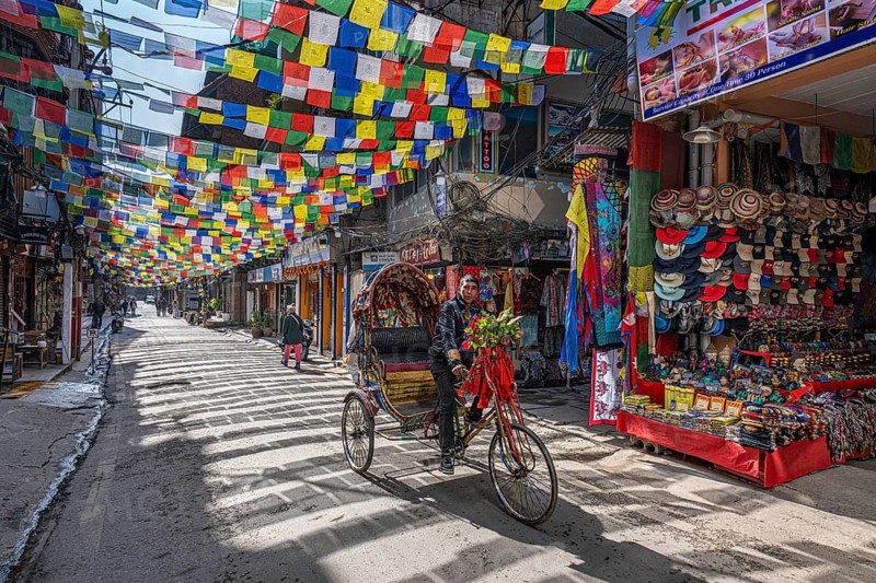 Bicycle rickshaw in a sparsely busy street with prayer flags and souvenir shops, Thamel, Kathmandu, Nepal