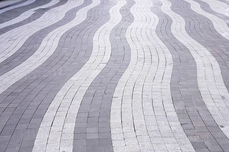 Curved lines of gray and white paving stones create an eye-catching pattern on an urban walkway. This modern design offers visual interest and enhances the pedestrian experience in the area