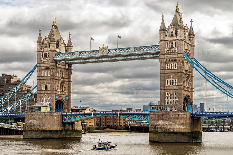 The Victorian bascule towers of Tower Bridge rise above the River Thames as a river police patrol boat passes beneath the blue painted walkways, London, England, United Kingdom