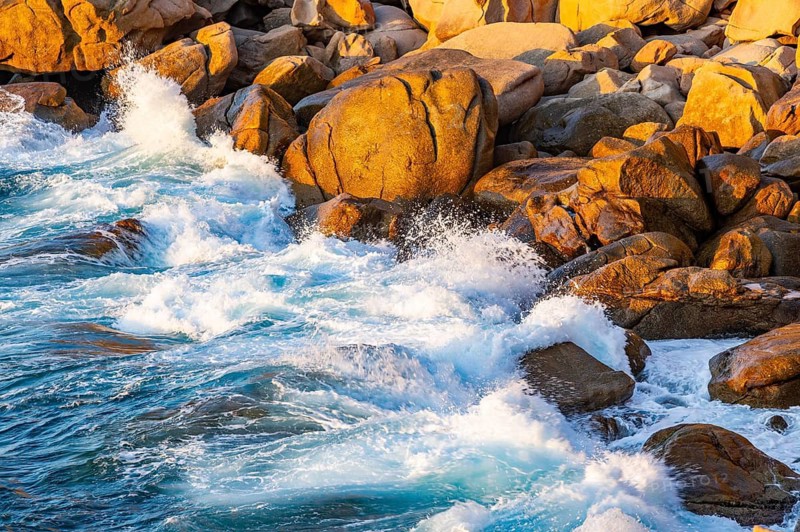 Surf at the coastline, blue water flows around the stones at Costa Paradiso in eveneing light, Sardinia, Italy