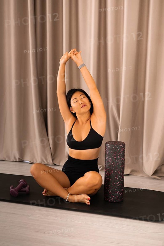 Woman in cross-legged pose, stretching with foam roller, expressing serenity and concentration