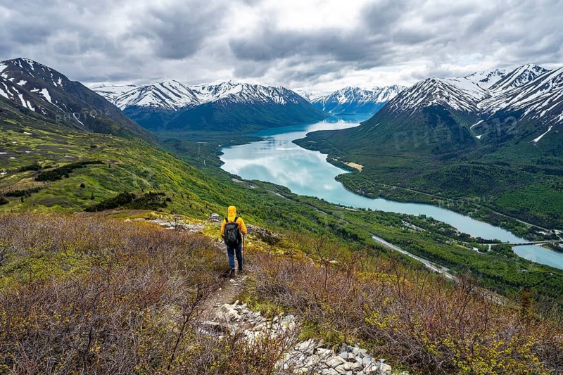 Climbers on a hiking trail on Slaughter Ridge, views of snowy mountains in spring and turquoise Lake Kenai Lake, Cooper Landing, Kenai Peninsula, Alaska, USA