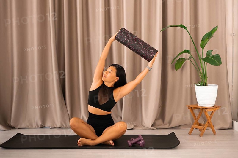 Tranquil scene of a woman stretching with a foam roller, adorned by an indoor plant