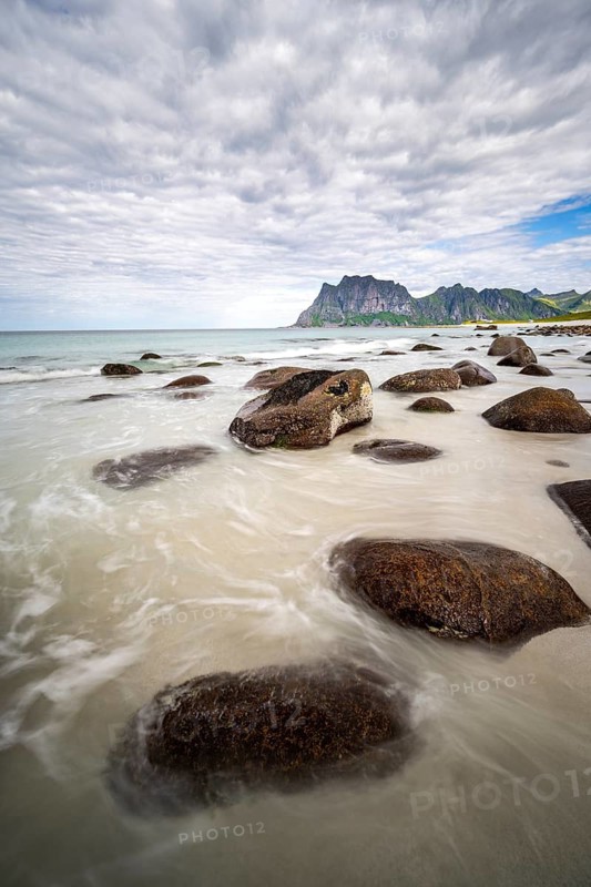 Rocks on Uttakleiv sandy beach, coast and blue sea, long exposure, rocky mountain peaks, Vestvågøya, Lofoten, Nordland, Norway