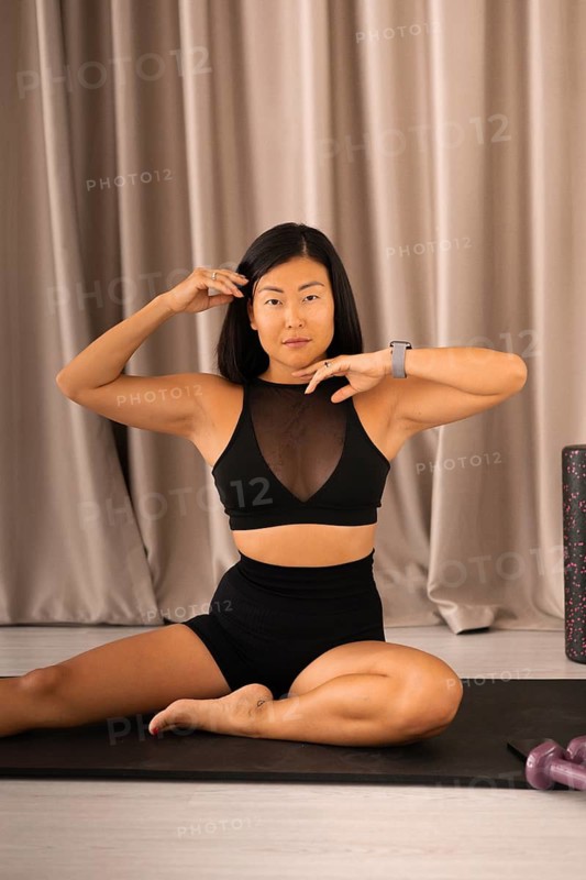 Woman seated on a yoga mat, posing with hands near her face during a workout routine