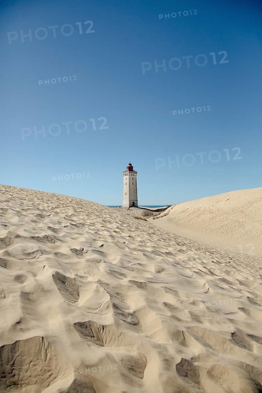 A lighthouse stands majestically surrounded by sand dunes under clear blue skies, lighthouse in the Rubjerg Knude hiking dune, Jutland, Denmark