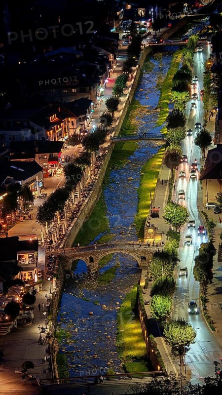 Night view of an illuminated river with bridges across Prizren Bistrica, with parallel roads, car traffic and a bridge, Prizren, Kosovo