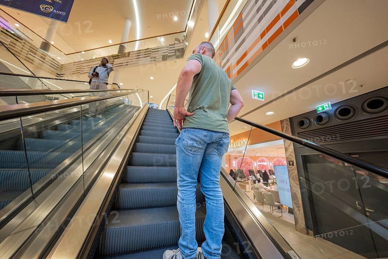 Man standing on escalator in a brightly lit shopping center, Milaneo, Stuttgart, Germany