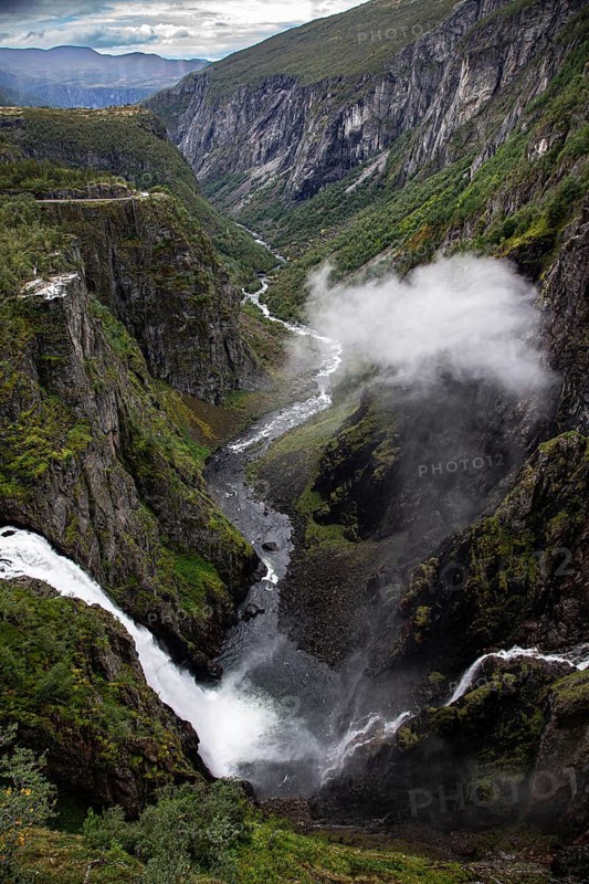 Dynamic waterfall in a steep gorge, surrounded by green vegetation and fog, Voringsfossen, with 165m drop height, above the village of Eidfjord, Hardangerfjord, Norway, Scandinavia