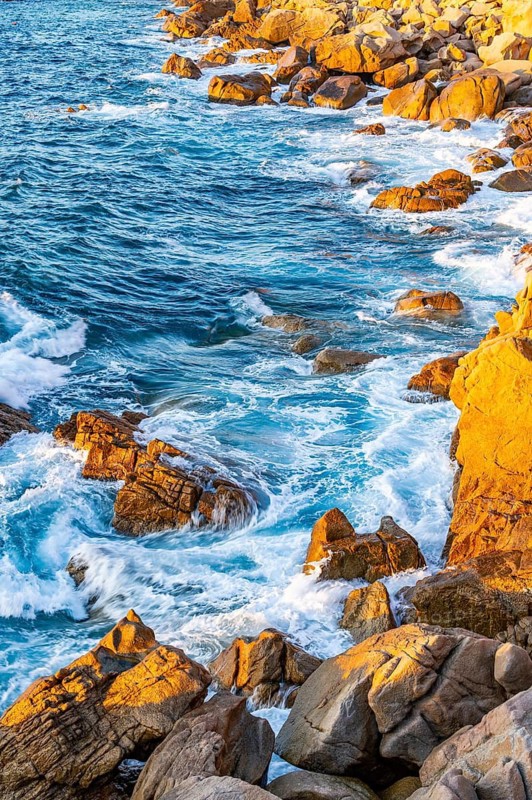 Surf at the coastline, blue water flows around the stones at Costa Paradiso in eveneing light, Sardinia, Italy
