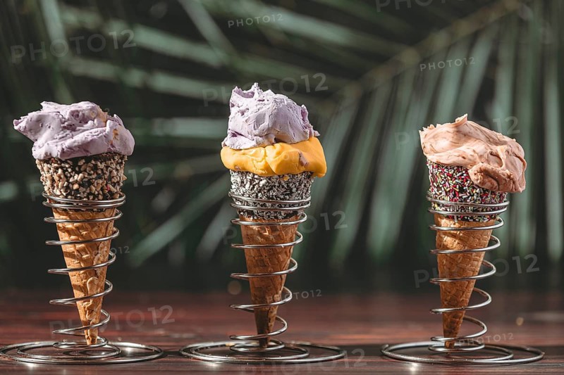 Three ice cream cones in metal holders against a tropical background