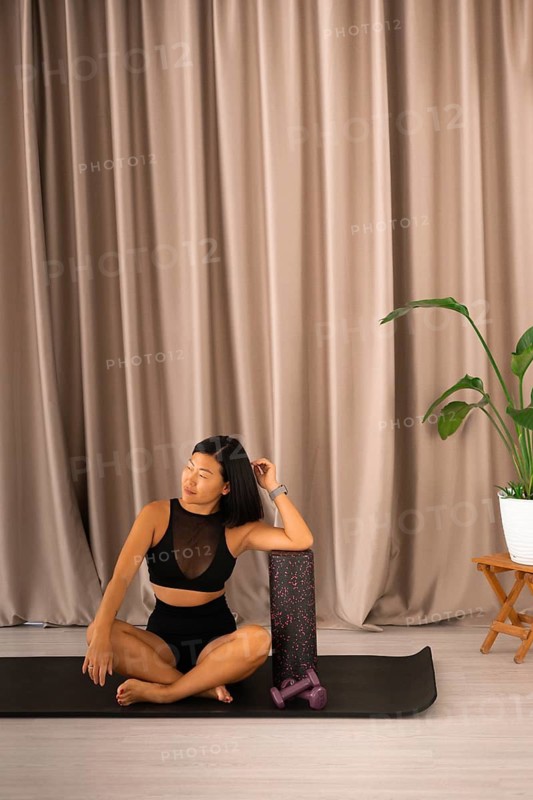 Woman meditates on a yoga mat beside a foam roller and plant, creating a serene atmosphere