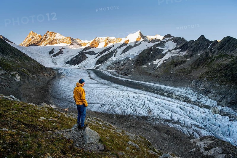 Young man in front of impressive high-alpine landscape, Finsteraarhorn and Agassizhorn mountain peaks with alpine glow at sunrise, Upper Arctic Ocean glacier, Bernese Alps, Bernese Oberland, Switzerland