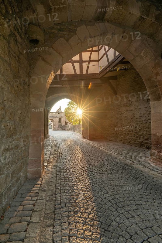 20 August 2026, Sunlight shines through the historic archway of the medieval town gate in Iphofen, Bavaria, Germany