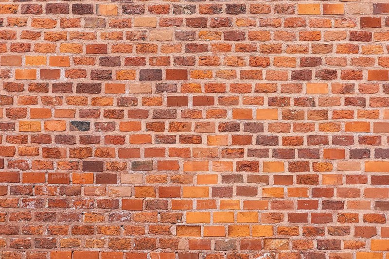 A textured wall made of red and brown bricks. The bricks vary in size and color, creating a rustic appearance. Ideal for backgrounds or architectural designs