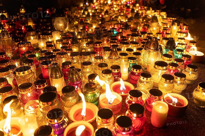 Candles glowing in colorful jars at night vigil in cemetery. A huge number of multicolored burning candles and lamps at a cemetery during All Saints' Day celebrations. Warsaw, Poland