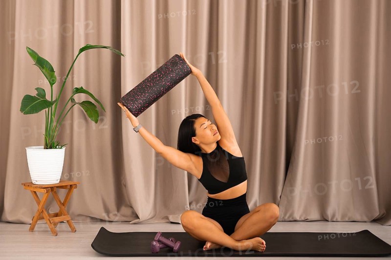 The woman, in a yoga pose, stretches with a foam roller, surrounded by a serene setting
